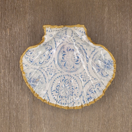 A scallop-shaped ceramic dish with a blue floral pattern and a gold ruffled edge, photographed from above on a brown wood-grain surface.