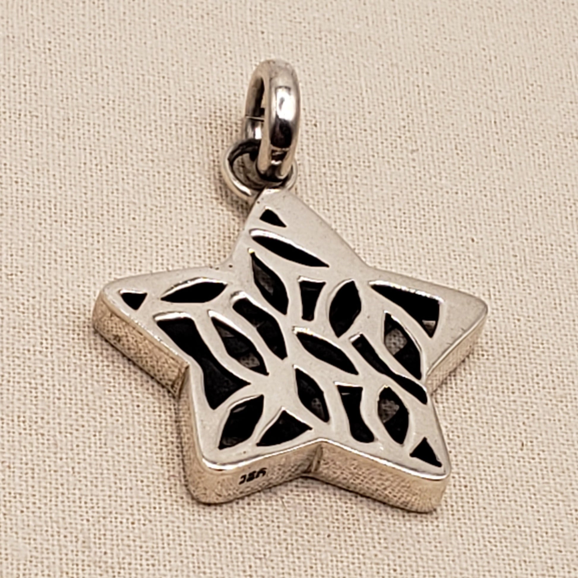 Silver Hamsa pendant with black cut-out design on a beige fabric background